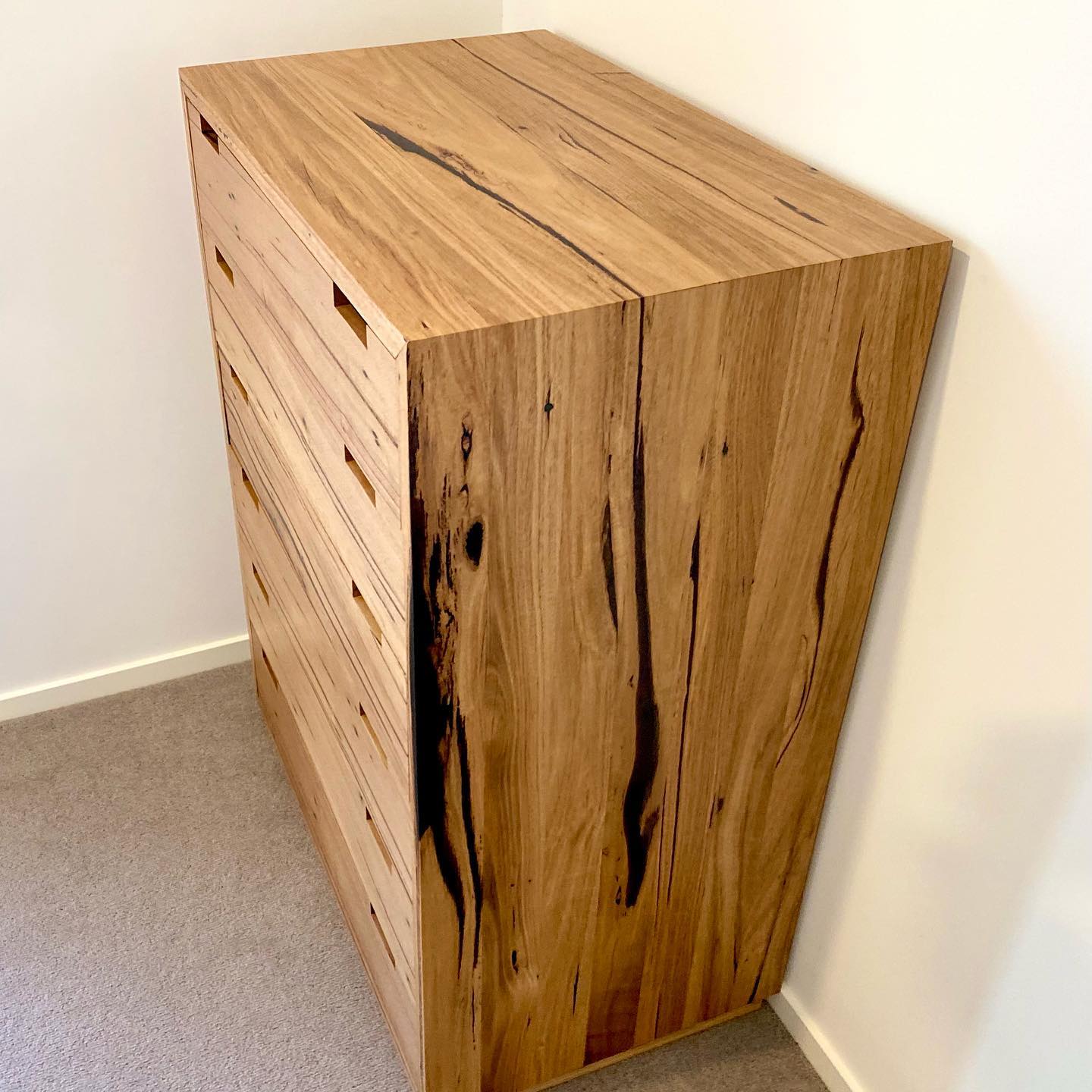 Solid timber tallboy with natural grain detail and minimalist handle cutouts.