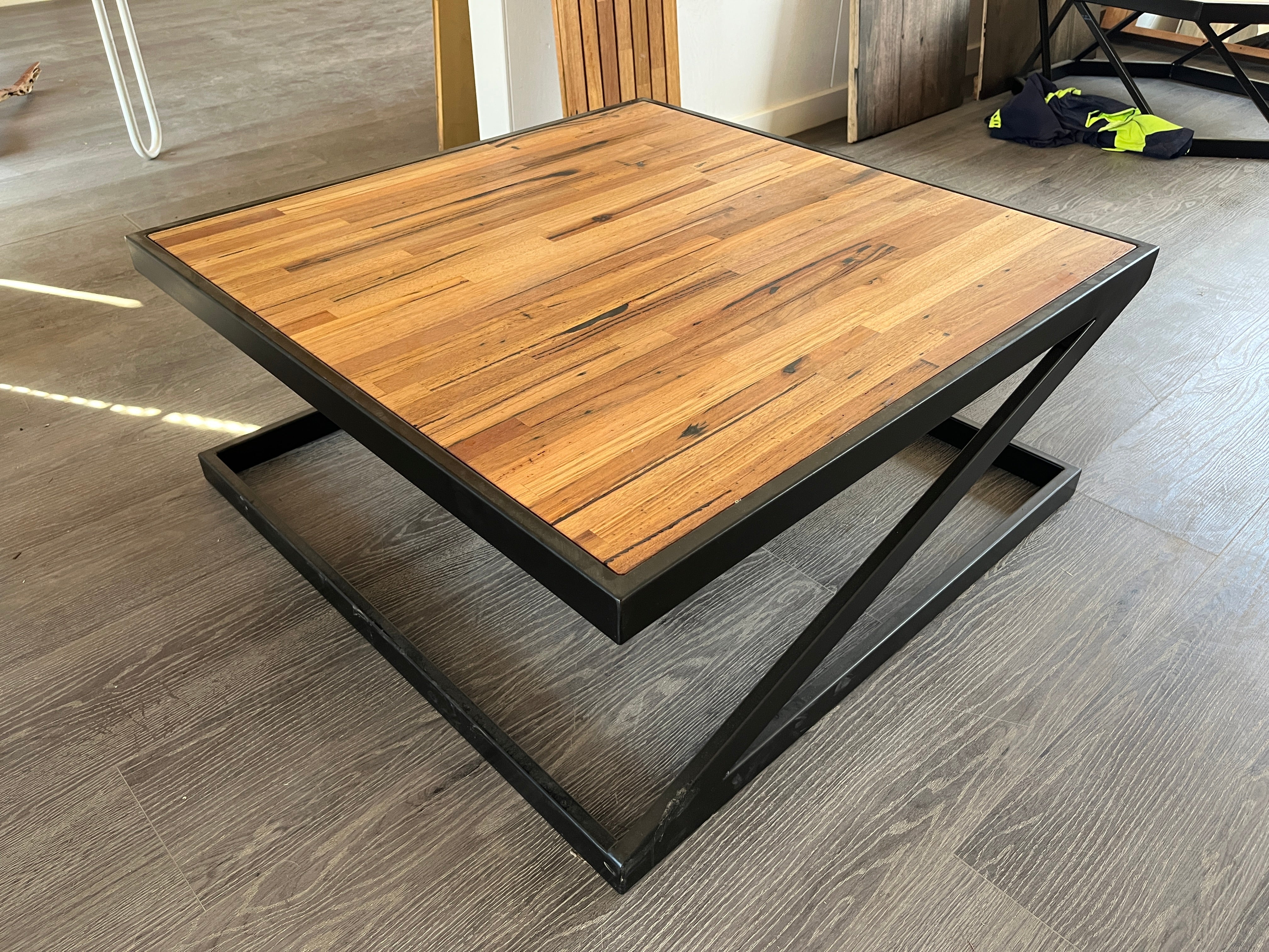 Square coffee table with recycled timber top and black powder-coated metal frame in industrial Z design.