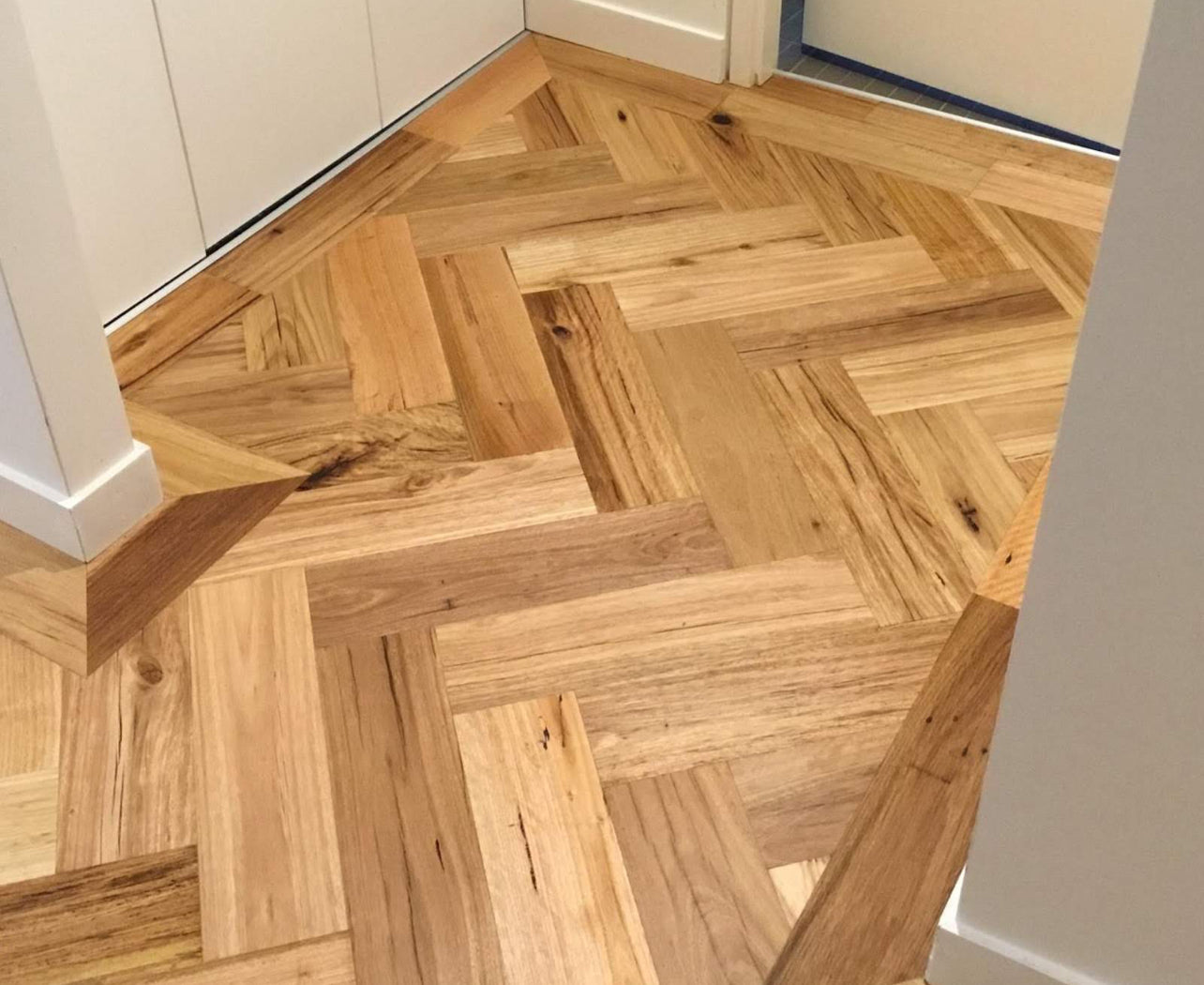 Close-up view of recycled engineered herringbone hardwood flooring in a hallway with clean joinery.
