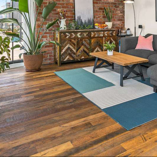 Living room with rough sawn recycled timber flooring, exposed brick wall, indoor plants, and modern grey sofa