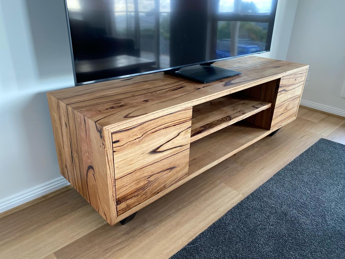 Freestanding solid spotted gum entertainment unit with open shelving and two doors, natural timber finish.