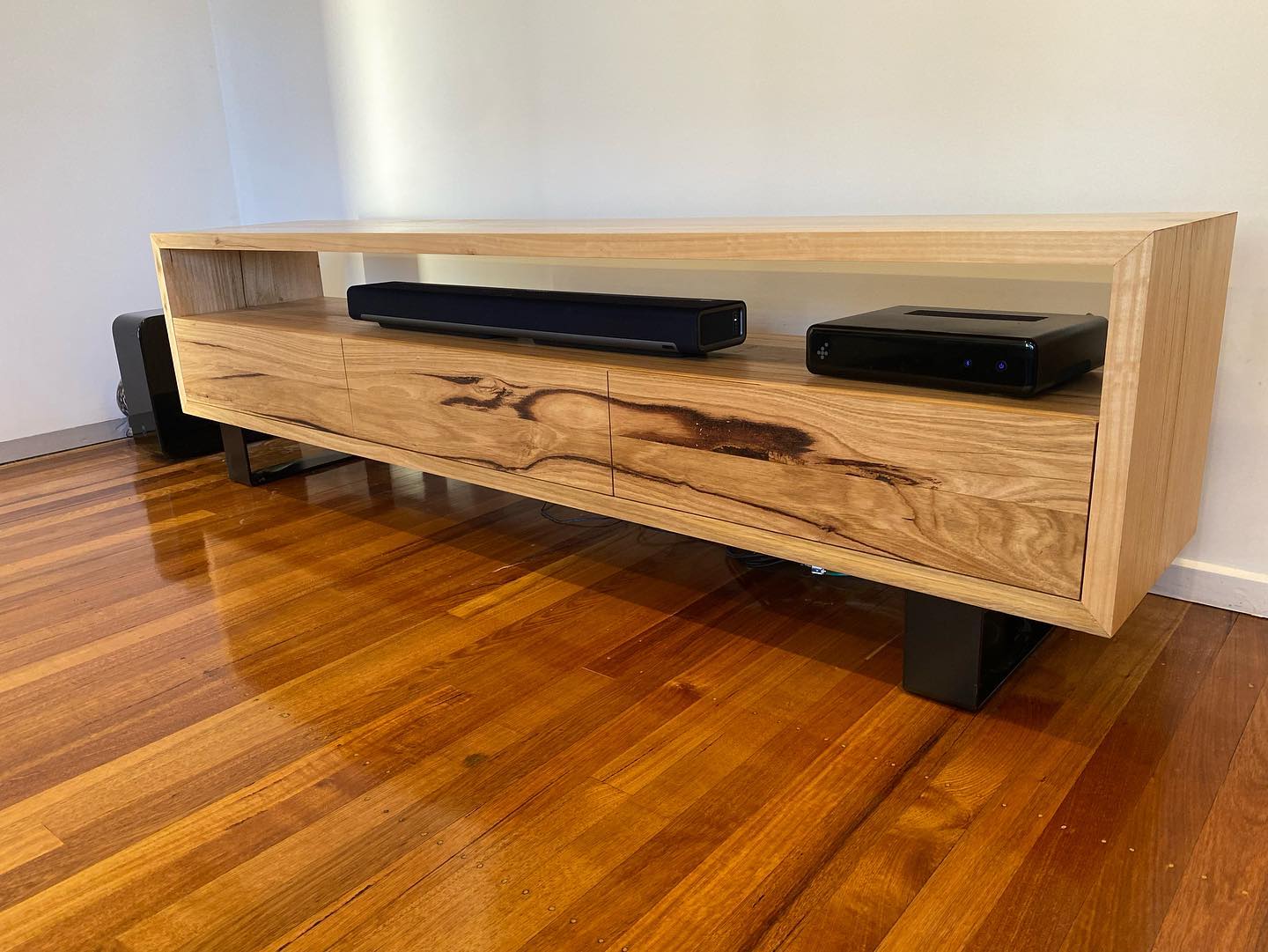 Timber entertainment unit with open shelf design and black metal legs, featuring bold natural grain pattern.